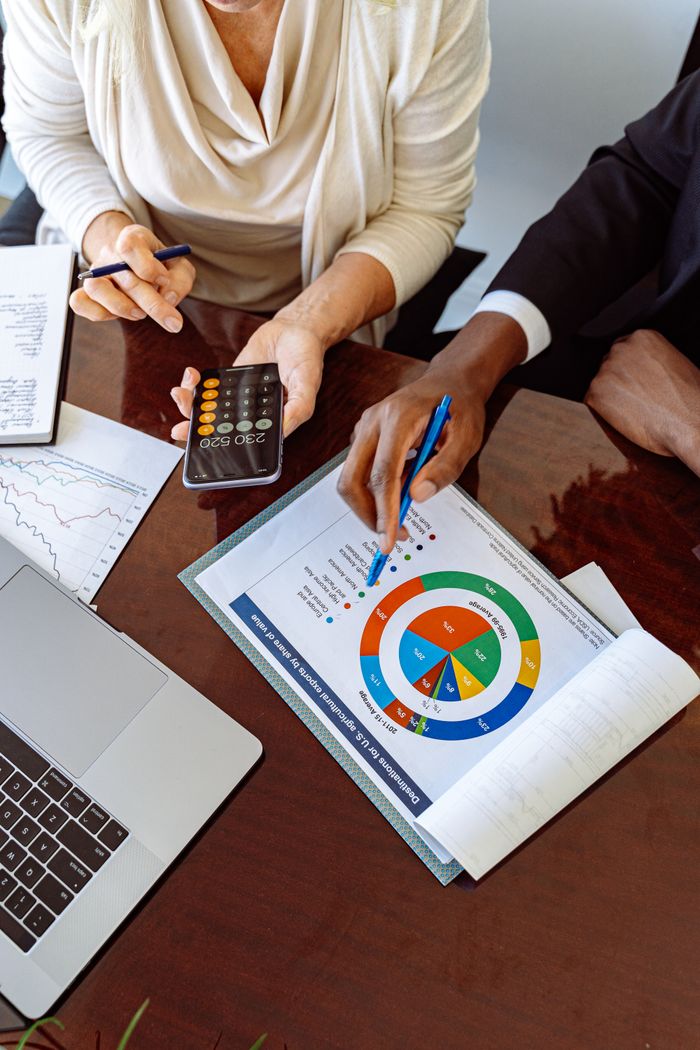 our-mission Two business professionals discussing financial documents and strategies at an office desk.